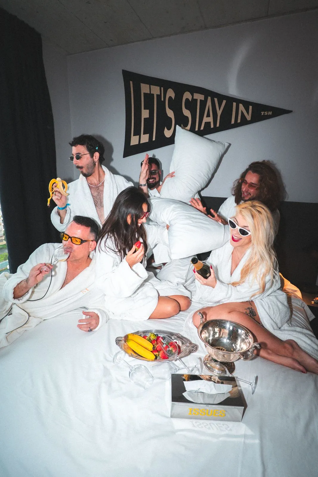 Foto de grupo en una cama con el cartel Let's stay in